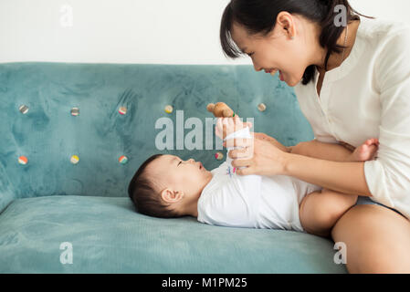 Il bambino e la madre figlia gioca, avvolgente, kissing a casa sul lettino Foto Stock