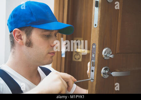 Giovani tuttofare in uniforme cambiando la serratura della porta. Foto Stock