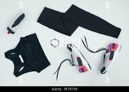 Piatto con laici sportswear con le scarpe da ginnastica e fitness tracker e sport bottiglia isolato su grigio Foto Stock