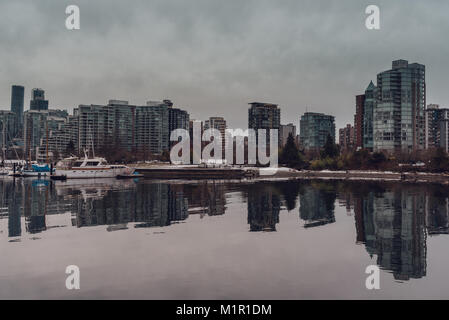 Vista del porto e Vancouver (BC, Canada) città di grattacieli con riflessi nell'acqua in un nuvoloso giorno d'inverno. Foto Stock