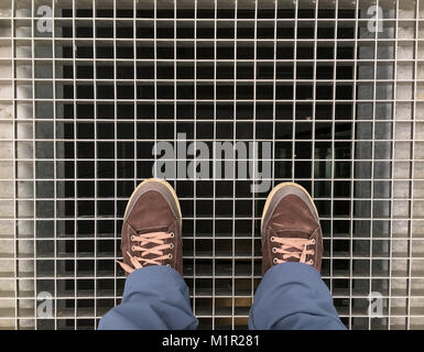 Piedi con le scarpe marrone in posizione eretta sul traliccio metallico al di sotto del quale è il pozzo di ascensore Foto Stock