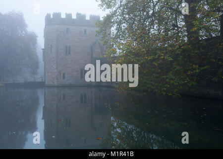 La guardiola medievale al Palazzo del Vescovo si riflette nel fossato e avvolta nella nebbia fitta su una mattina di novembre, pozzi, Somerset, Inghilterra. Foto Stock