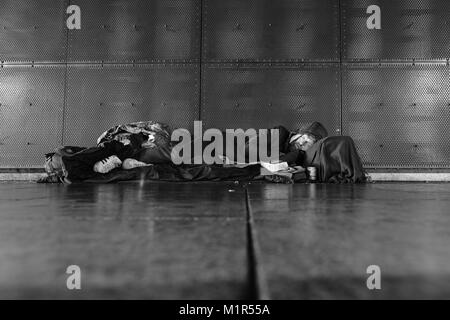 Un senzatetto uomo dorme sul duro freddo pavimento di cemento sotto Leeds stazione ferroviaria Foto Stock