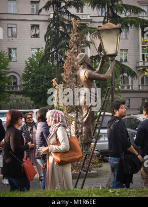 I pedoni sulla strada Baratashvili a Tbilisi, capitale og Georgia, passando da una scultura in bronzo di un uomo di illuminazione un vecchio lampione a gas Foto Stock