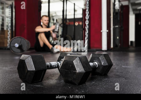 Close-up di una coppia di manubri con uomo rilassante in background Foto Stock