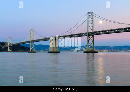 San Francisco-Oakland Bay Bridge con Full Moon Rising e rosa e blu Cielo di tramonto. Foto Stock