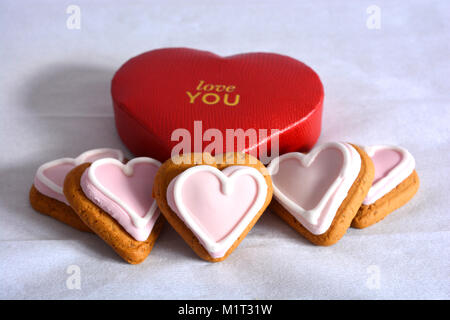 Un cuore rosso scatola sagomata con goffrato con amore è in oro di scritte e cinque rosa a forma di cuore gingerbread cookie Foto Stock