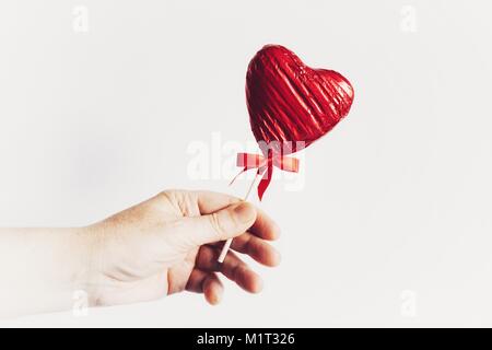 Donna che mantiene un rosso di stagnola avvolto lecca-lecca di cioccolato, un regalo speciale per il giorno di San Valentino. Foto Stock