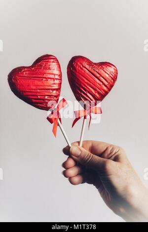Donna che mantiene rosso di stagnola avvolto il cioccolato lecca lecca, doni speciali per il giorno di San Valentino. Foto Stock