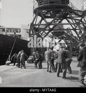 Degli anni Cinquanta, storico, maschio dockers tirando una corda per legare la RMS Queen Elizabeth ocean liner in a Southampton docks, Inghilterra, Regno Unito. Chiamato dopo la British Regina Madre, è stata la più grande nave passeggeri mai costruito in quel momento (1938) e rimase per 56 anni. Essa è stata utilizzata come un troopship durante il WW2 e solo divenne un ocean liner come previsto nel 1946. Foto Stock