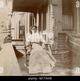 Antique circa 1905 fotografia, donna in una sedia a dondolo sul suo portico. Posizione sconosciuta, probabilmente la Nuova Inghilterra, Stati Uniti d'America. Ho più foto di questa famiglia a Riggsville (ora Robinhood), Maine in Sagadahoc County, Stati Uniti d'America. Foto Stock