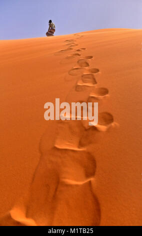 Tracce di persona sulla sabbia arancione nel deserto, la persona in abiti svolazzanti a va a una duna Foto Stock