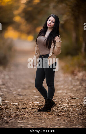 Bella giovane donna waering abiti casual in posa nella foresta, corpo pieno shot con estrema profondità di campo Foto Stock