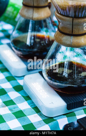 Versare il caffè gocciola in vetro artigianale da produttori di birra seduti sulle bilance elettroniche mentre all'aperto su un tavolo da picnic Foto Stock