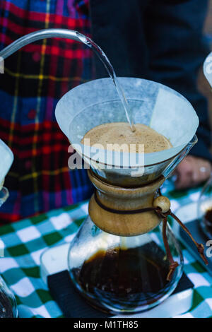 Barista versa acqua bollente fron bollitore specializzati a versare il caffè in vetro artigiano birraio mentre all'aperto Foto Stock