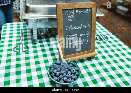 Bocce di frutta da un segno pubblicità Buongiorno pancake con una senza glutine opzione. Persona prepara frittelle in background Foto Stock