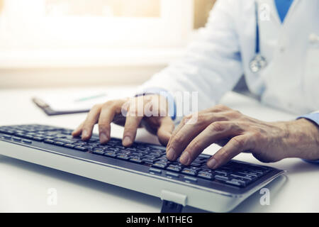 Medico digitando sulla tastiera del computer in ufficio. consultazione online Foto Stock