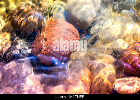 Macro shot di magiche, mare di guarigione di ghiaia e rocce, bianco e bolle di schiuma nella colorata e vibrante di acqua oceanica pieno di energia. Raggi di sole, riflessioni Foto Stock