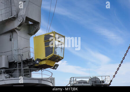 Colpo di giallo cabina di comando con il lavoratore. Vecchie e arrugginite, porta grigia gru di sollevamento carico in nave sul cielo blu chiaro dello sfondo. Attrezzature per la nave di scarico Foto Stock