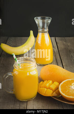 Mango e il succo di arancia in mason jar e fetta di frutta tropicale su un tavolo di legno. Fresco e salutare drink tropicali. Close up. Foto Stock