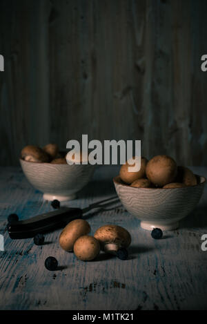 Foto verticale con diversi funghi marrone. Alcuni di loro sono in ciotole di ceramica. Altri gli champignon sono versate su vintage tavola di legno con pochi blackth Foto Stock