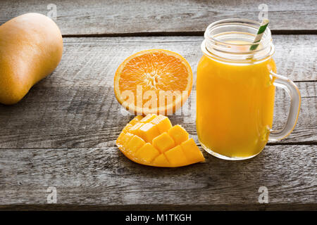 I frullati di frutta tropicale: mango, arancio in un vetro mason jar sul vecchio tagliere in legno. Foto Stock