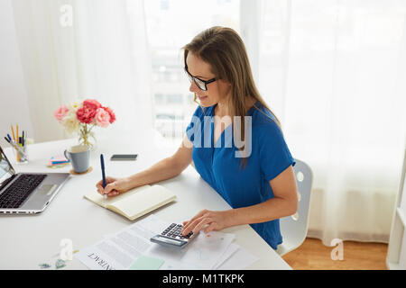 Donna con la calcolatrice e notebook in ufficio Foto Stock