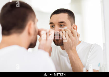 Giovane uomo di applicare la crema per il viso a bagno Foto Stock