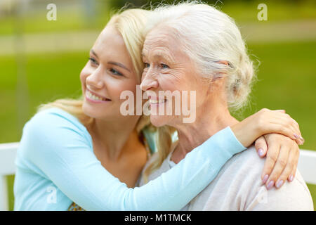 Figlia di madre senior avvolgente su una panchina nel parco Foto Stock