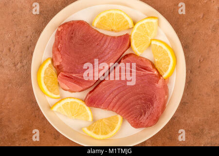Crudo fresco crudo Pinna Gialla Filetti di Tonno con le fette di limone contro uno sfondo rosso Foto Stock