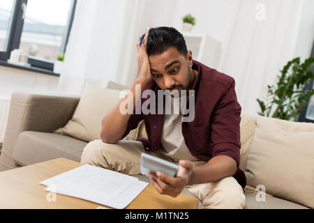 Uomo confuso con documenti e calcolatrice a casa Foto Stock
