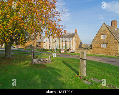 Il grazioso villaggio verde in Eydon, Northamptonshire, Regno Unito; con alcune vecchie scorte di legno e in primo piano di un vecchio boxed nel montante. Foto Stock