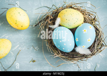 Uova di Pasqua nel nido di uccello blu su sfondo di legno. Decorate le uova di pasqua con piume nel nido sul vecchio tavolo in legno con copia spazio. Primavera, Pasqua o Foto Stock