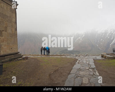 Gergeti Trinity Church di alte montagne del Caucaso in Georgia, isolata su una cima, nuvoloso ed umido, i turisti a Viewpoint Foto Stock