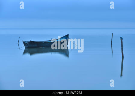 Lonely barca sul lago grande nella nebbia, blu ora prima dell'alba Foto Stock