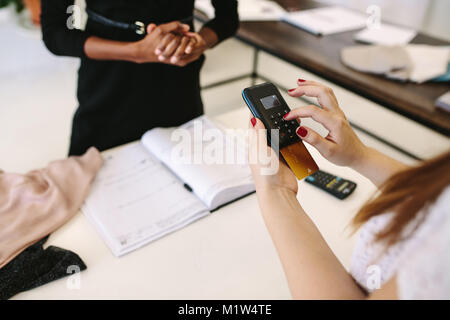 Acquisti del cliente usura designer presso una boutique di moda. Ritagliato shot del cliente che effettua il pagamento digitando il suo pin nel punto di vendita della macchina. Foto Stock