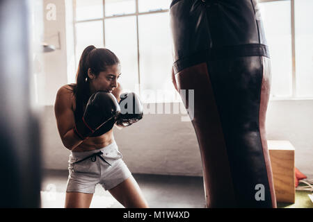 Boxer femmina di colpire un enorme sacco da boxe presso un studio di inscatolamento. Donna boxer allenamento duro. Foto Stock