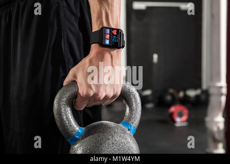 Close-up di un atleta giovane uomo che indossa Smart Watch Holding bollitore campana in palestra Foto Stock