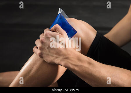 Close-up di una persona che chieda il sacchetto del ghiaccio su un ginocchio infortunato in palestra Foto Stock