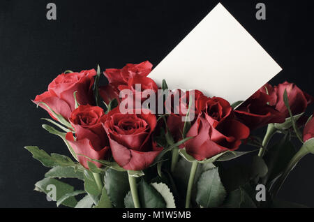 Un mazzo di rose rosse in un raggruppamento verticale con vuoto bianco scheda messaggio a livello degli occhi. Sfondo nero. Foto Stock