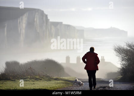 Signora cani a piedi nella nebbia vicino la mitica sette sorelle chalk cliffs, East Sussex, Regno Unito Foto Stock