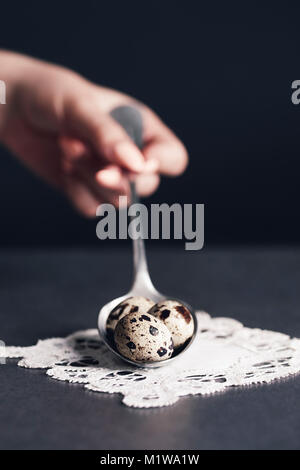Mano umana tenendo vintage cucchiai con uova di quaglia Foto Stock