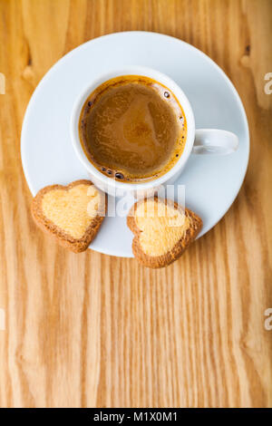 A forma di cuore biscotti e caffè su uno sfondo di legno. Colazione romantica. Biglietto di auguri per il giorno di San Valentino. Foto Stock