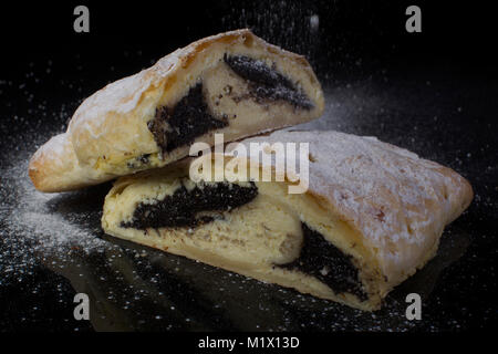 Strudel con semi di papavero spolverati con zucchero a velo tagliare close-up su sfondo nero Foto Stock