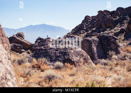 Donna sorge sulla sommità di una grande pietra nella Happy Boulder arrampicata su roccia area vicino Vescovo, California Foto Stock