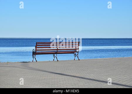 Sedile unico sul lastricato in pietra argine o località di mare sopra lo sfondo di colore blu acqua e cielo limpido, giornata soleggiata, vista posteriore Foto Stock