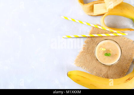 Frullato di banana con un tubo di carta e le foglie di menta. Le banane sono interi e tagliati su sfondo grigio Foto Stock