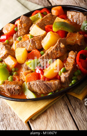 Cibo asiatico: Stufati di carne con patate e peperoni, piselli, pomodori e carote close-up su una piastra sul piano verticale. Foto Stock