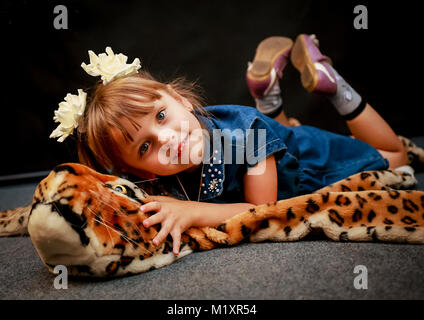 Su uno sfondo nero sulla pelle di un giocattolo di leopard si trova womens baby e sorridente Foto Stock