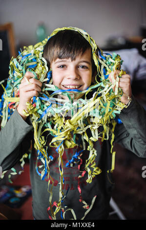 Bambino con streamers intorno al suo collo e la testa per la festa di carnevale in casa sua Foto Stock